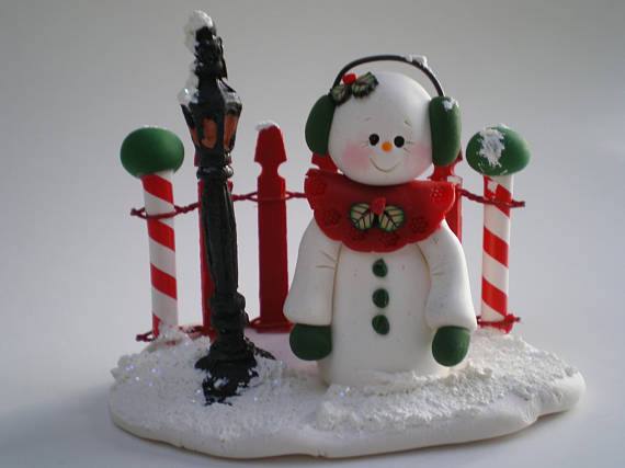 Winter landscape - Snowman standing on a snow covered base with a red snow capped fence and lamp post.