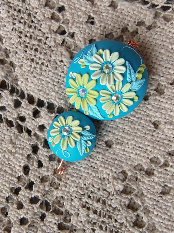 clay focal bead set on a summery turquoise background and flowers in shades of lime green and light turquoise