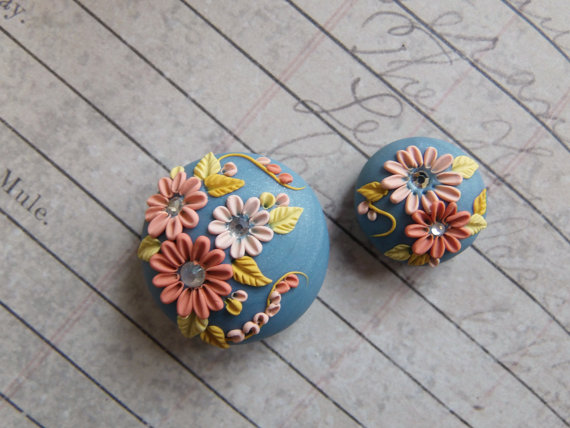 handcrafted bead on a silvery sky blue background, and floral and foliage in shades of yellow and corals. Each flower has a crystal center accent