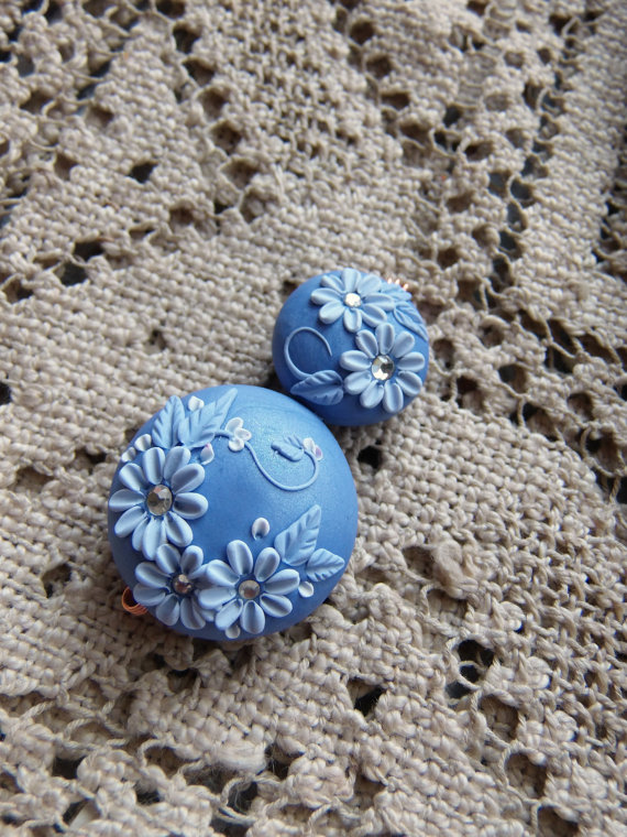 handcrafted flowers of this polymer clay floral embroider beads on a shimmery periwinkle background, and floral/foliage in various shades of periwinkle and white.