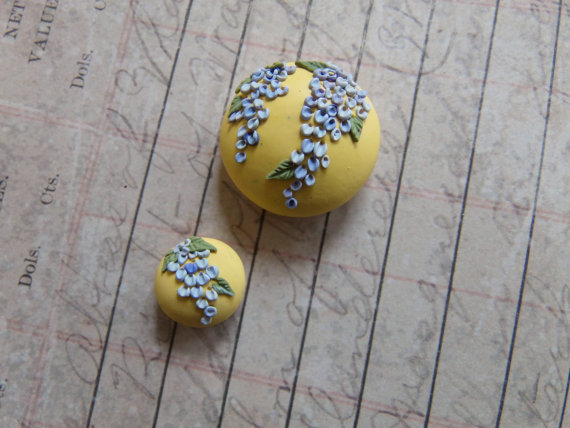 clay focal bead on a buttery yellow background, with wisteria in shades of lavender, and green foliage.