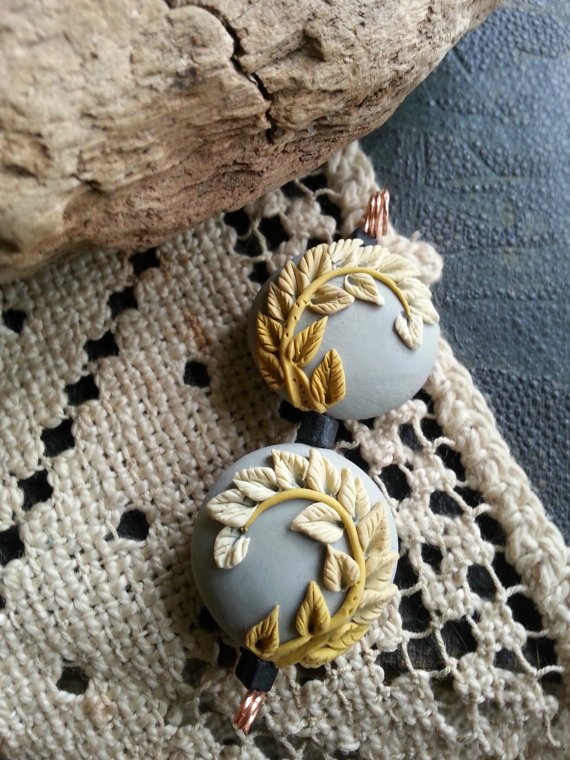 A pair of two artisan polymer clay focal beads. Grey background with shades of matte gold.