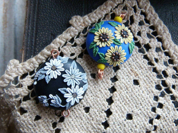 a pair of 2 handcrafted artisan beads one in shades of black/grey/white, the other in blue/yellow/green.