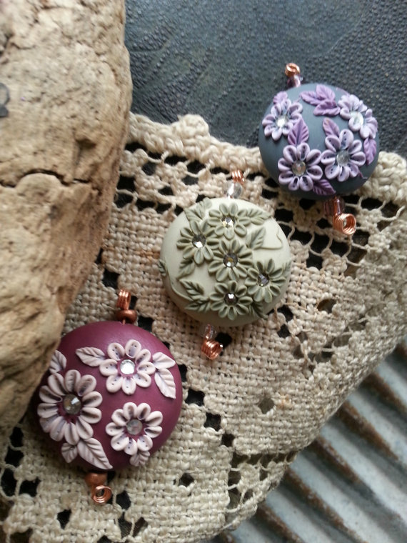 A trio of beads. The first one is in deep rose/pale pink, the second in dark & light sage green, and lastly shades of purple flowers on a deep grey background.