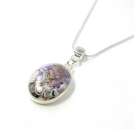 Polymer clay short necklace with its oval pendant, in grey, purple and orange tones, and pearls reflects.