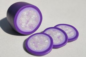 Polymer clay faux agate cane with purple layers and translucent crackled core, with three cut slices